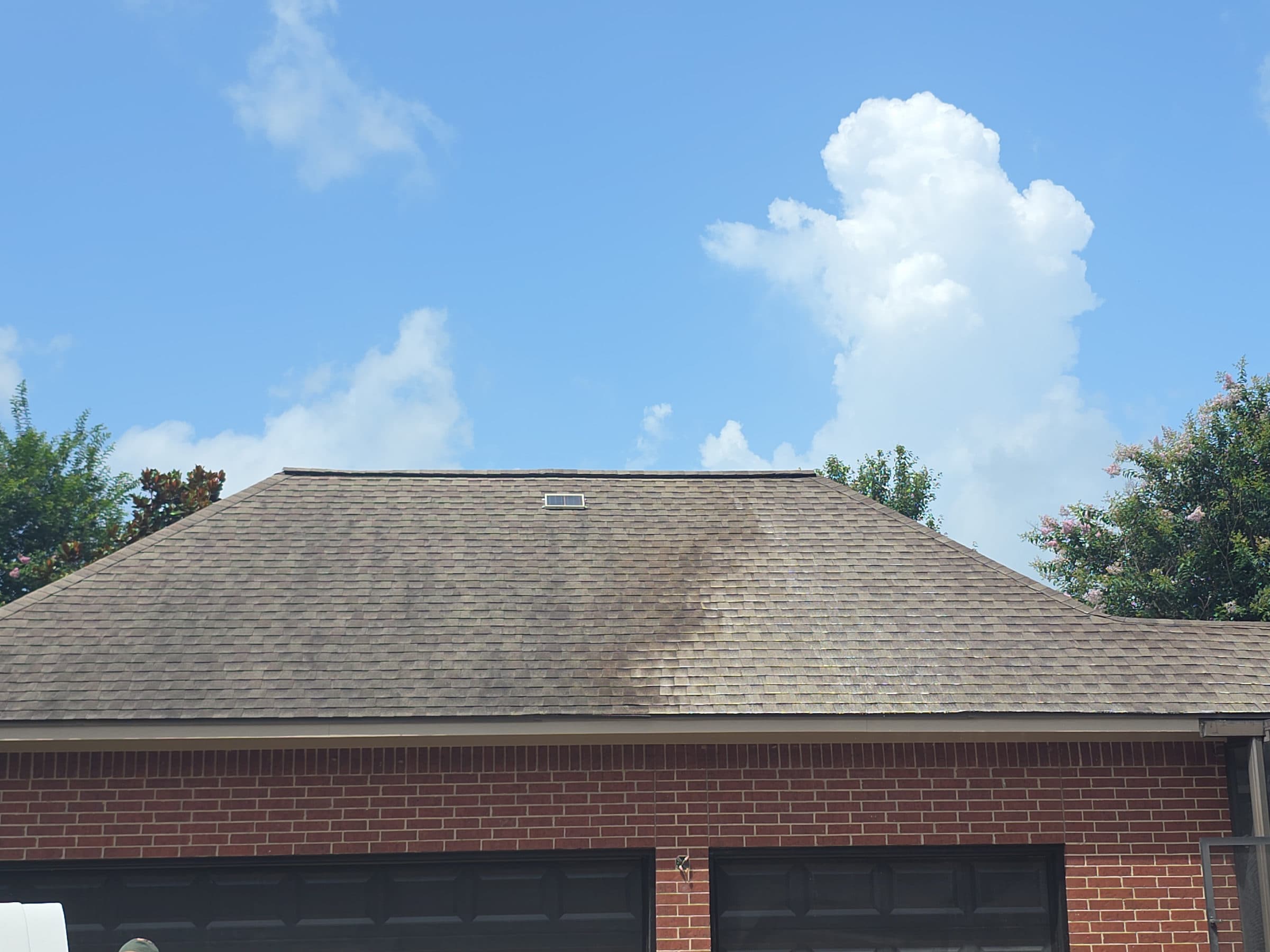 Soft washing in progress on a house exterior, detergent lifting growth at low pressure